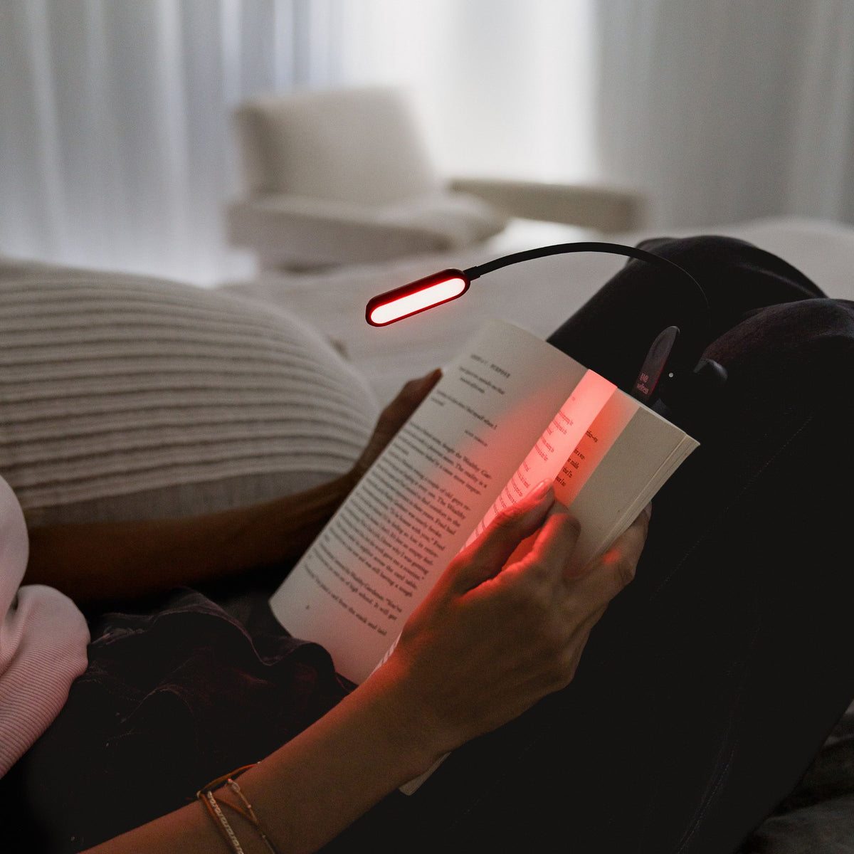 Woman reading in bed with LUM8 Wind Down Reading Light in red mode — sleep friendly book light
