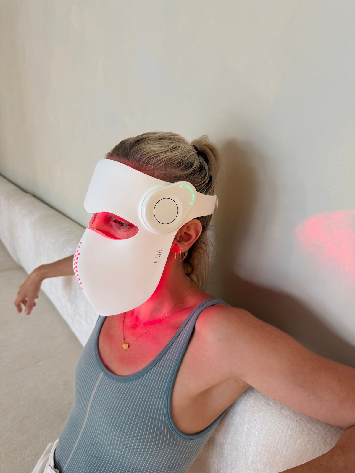 Woman relaxing on a linen sofa wearing the LUM8 ProLaser Face Mask in red light mode